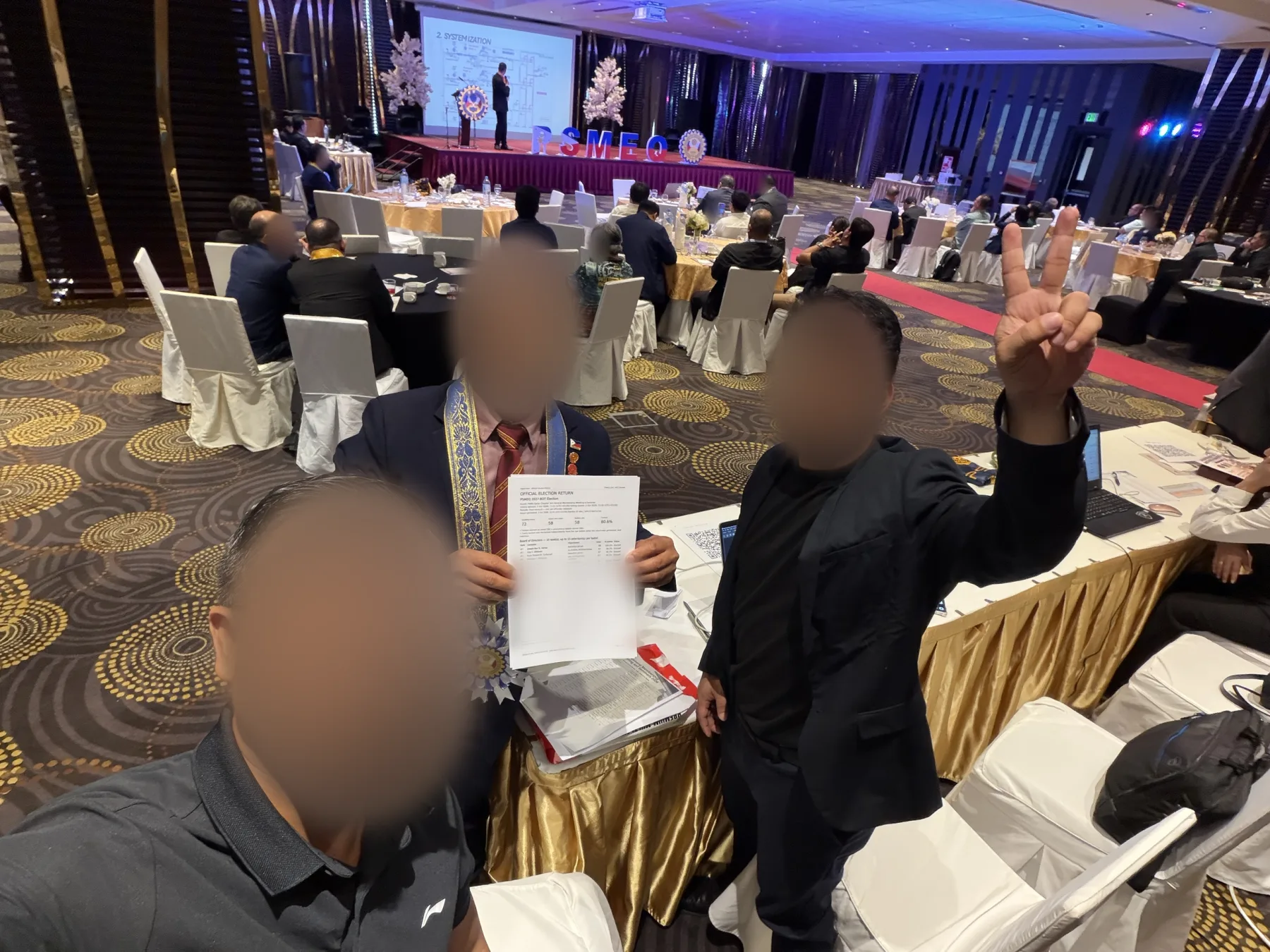 Three attendees holding an official election return in a ballroom during a general membership meeting
